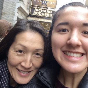 Two people smiling for a selfie outside the Richard Rodgers Theatre, with the Hamilton musical sign visible in the background.