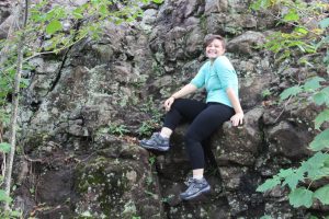Dani sitting on a rock wall formation with foliage
