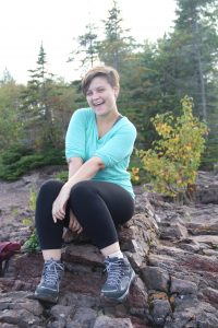 Dani sitting on a rock with pine trees in the background.