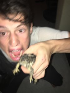 A surprised young person holding a toad in their hand, with a blurred, excited expression on their face. The image is slightly out of focus, adding to the chaotic and spontaneous feel.