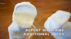 Two white sock puppets are shown facing each other with the text REPEAT WITH ANY ADDITIONAL SOCKS overlaid at the bottom. A blurred brown background and a small Camp Awesome logo appear in the top left corner.