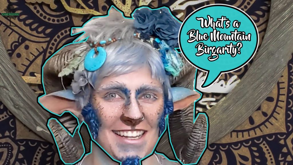 A person in fantasy makeup with blue accents, artificial horns, elf ears, and decorative accessories smiles. A speech bubble asks, Whats a Blue Mountain Burgarty? Decorative patterned background.