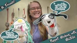 A woman with glasses smiles while holding two sock puppets. One puppet says, “Hi! My name’s Vessie!” and the other says, “…and I’m Scooter!” Text reads: “Hi Friends!” and “Puppet Making with Maddie.” Guitars hang on the wall behind.
