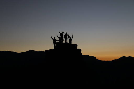 Silhouette Of Group Of Children Standing On Rock With Hands Up
