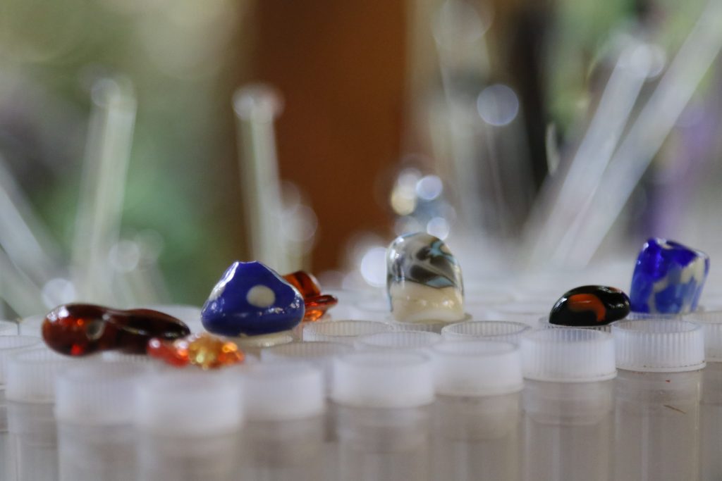 Colorful glass beads and stones are arranged on white plastic tubes, creating an abstract, artistic scene reminiscent of the vibrant crafts often enjoyed during family camp activities. The blurred background adds a soft, creative touch.